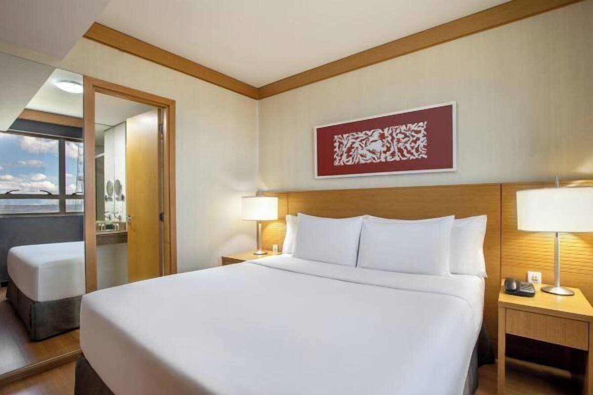 A hotel room with a large bed, two bedside tables, a mirror, and a red abstract artwork on the wall.