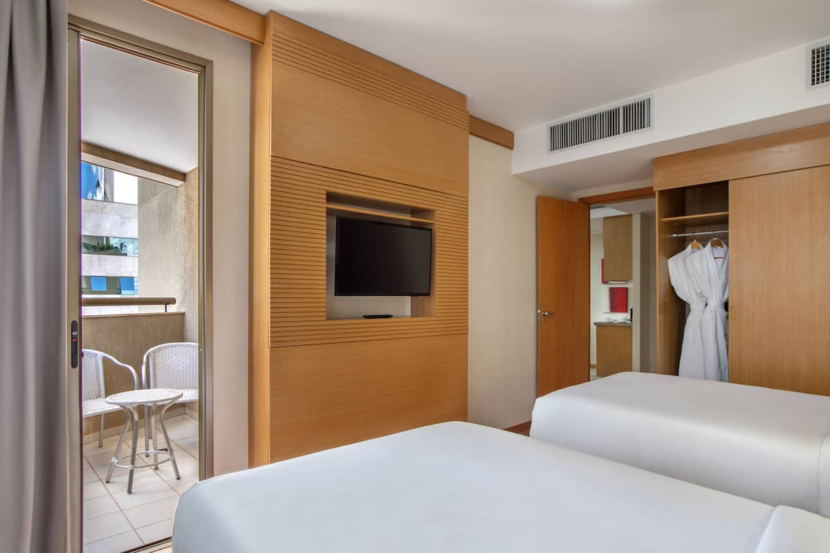 A hotel room with a bed, a TV mounted on the wall, a wardrobe, and a balcony with chairs.