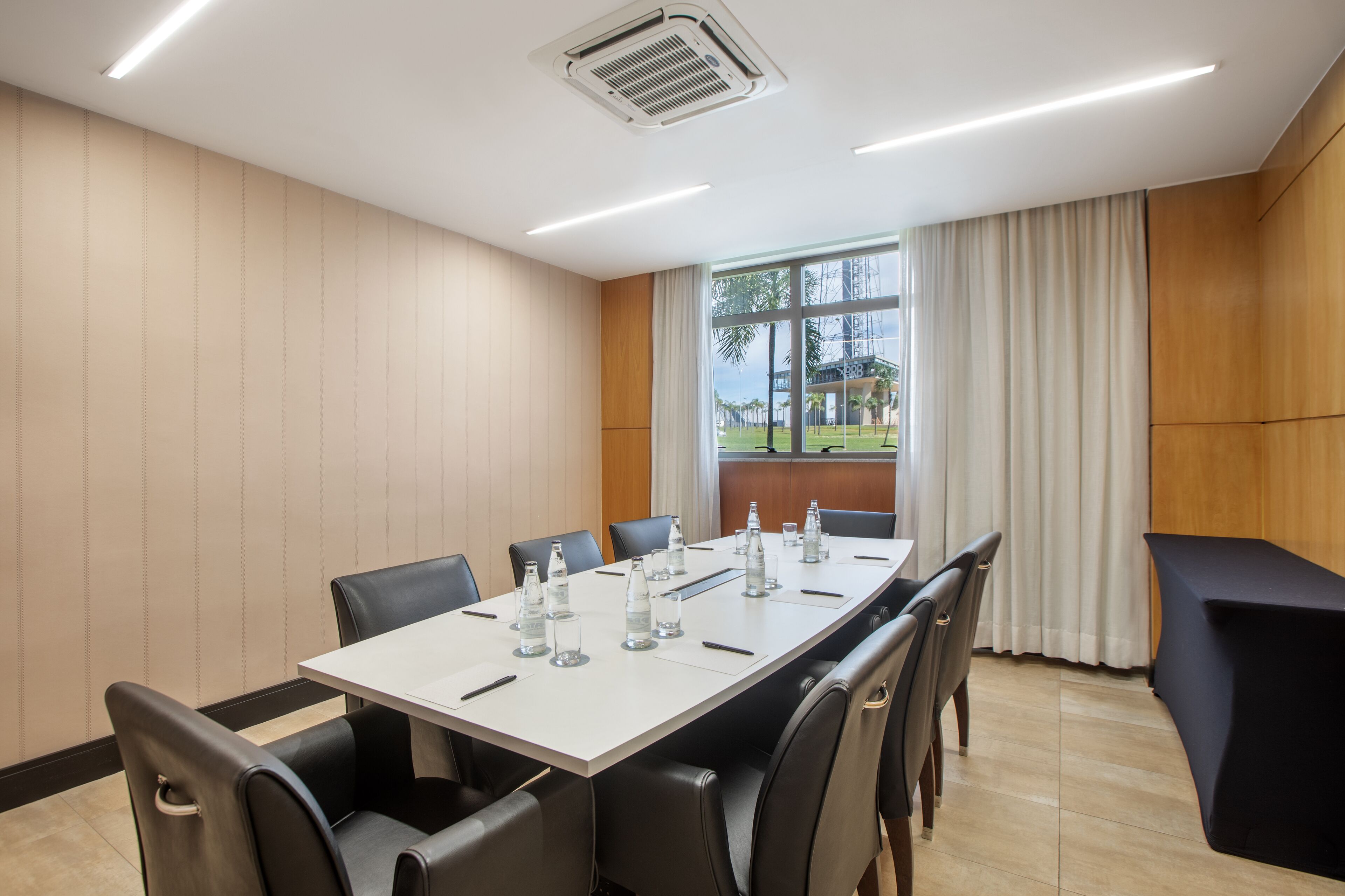 A conference room with a long table, black chairs, and a view of a garden through the window.