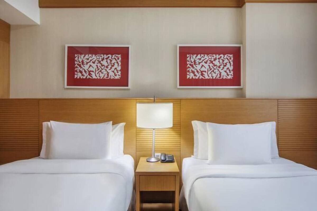 A hotel room with two beds, a nightstand with a lamp, and two framed wall art pieces.