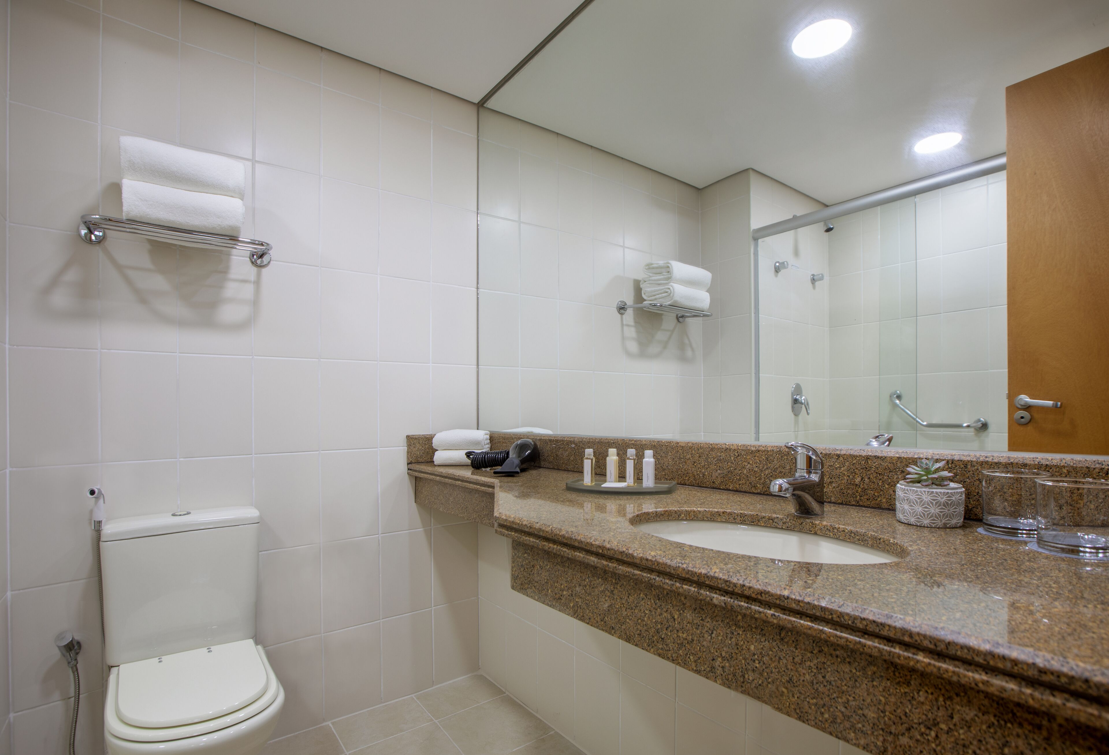 Un baño moderno con inodoro, lavamanos y espejo. Hay toallas y artículos de aseo en el mostrador.