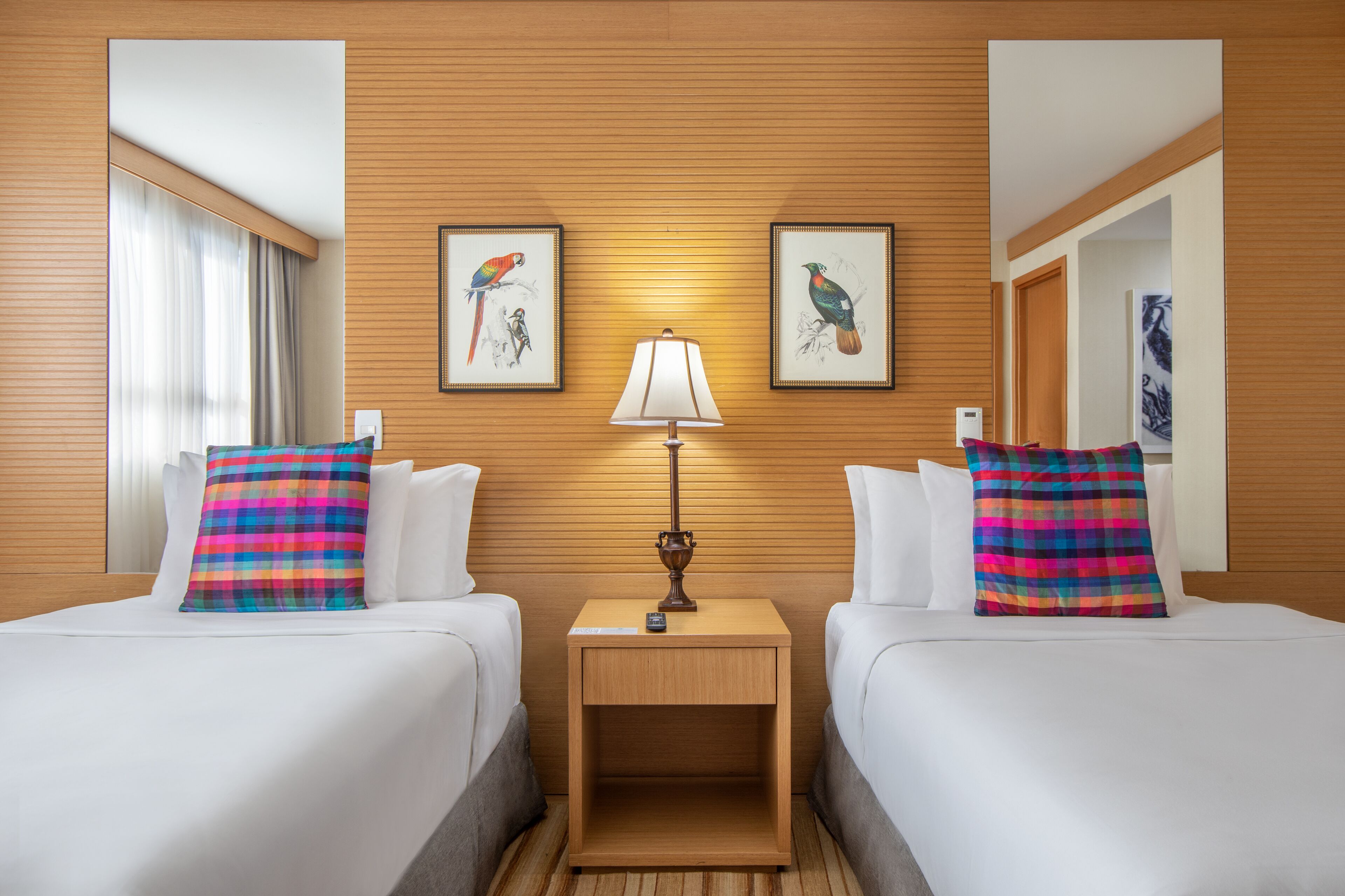 A hotel room with two beds, a nightstand with a lamp, and two framed pictures on the wall.