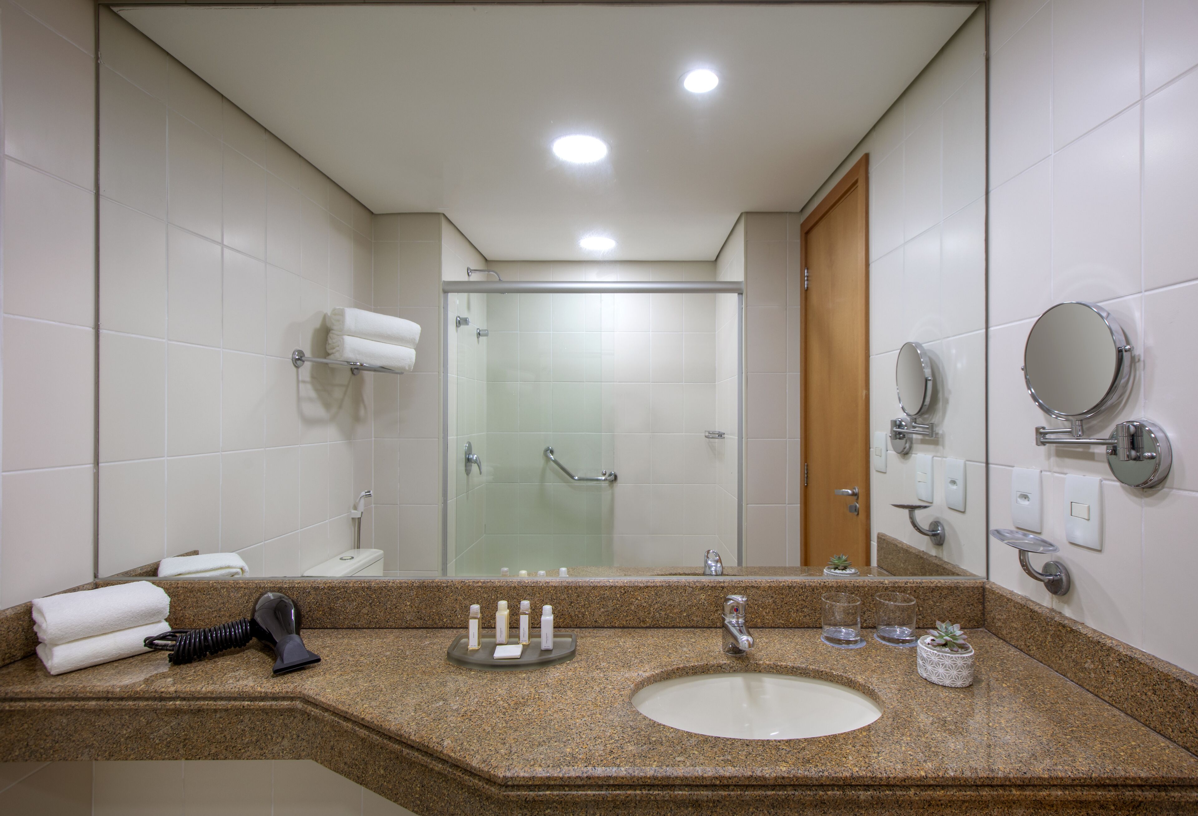 A bathroom with a granite countertop, a sink, a mirror, a glass shower enclosure, and a towel rack.