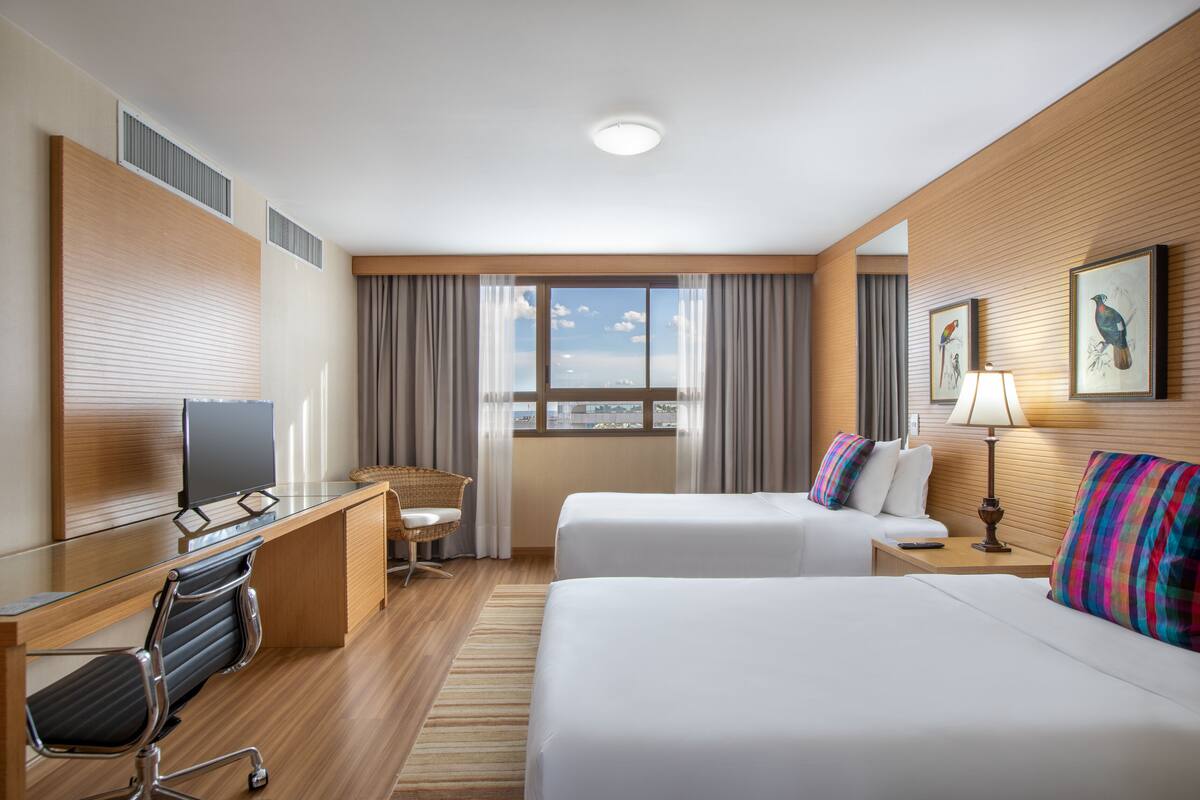 A hotel room with two beds, a desk with a computer, a chair, and a window with curtains.