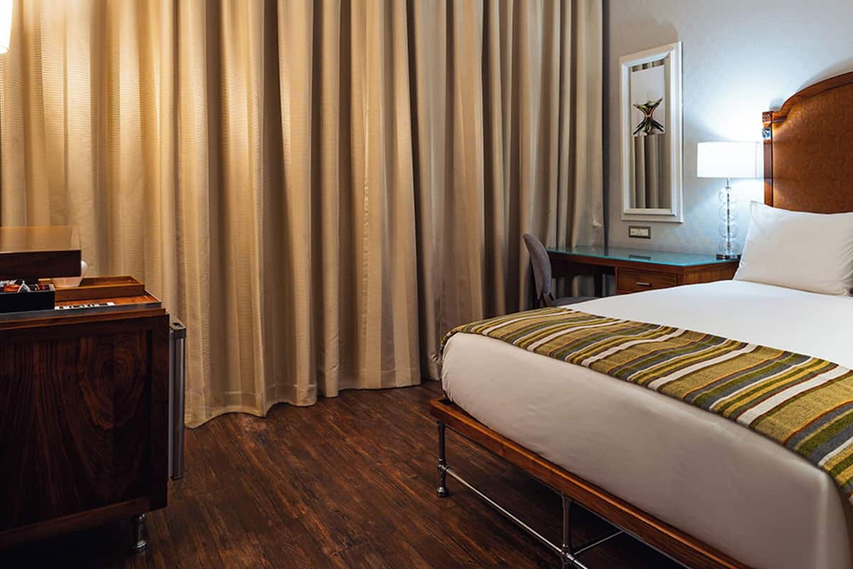 Una habitación de hotel con una cama de madera, un escritorio, una silla, una lámpara y un espejo.