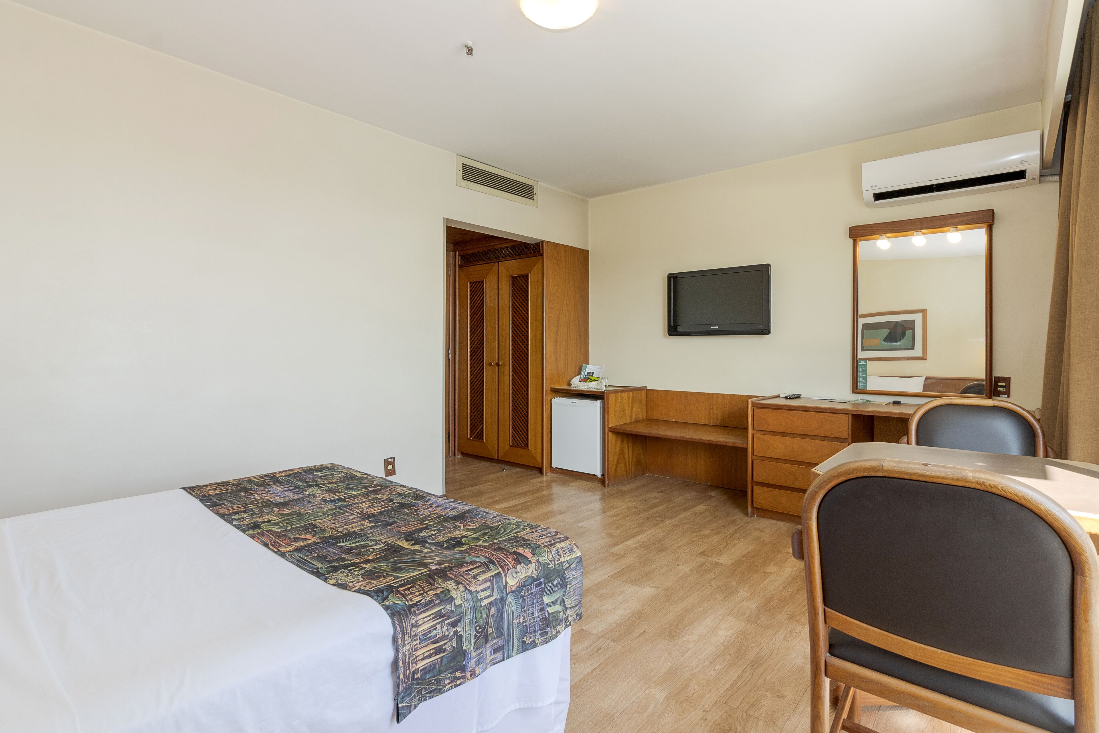 A hotel room with a bed, a desk, a chair, a television, and a mirror.