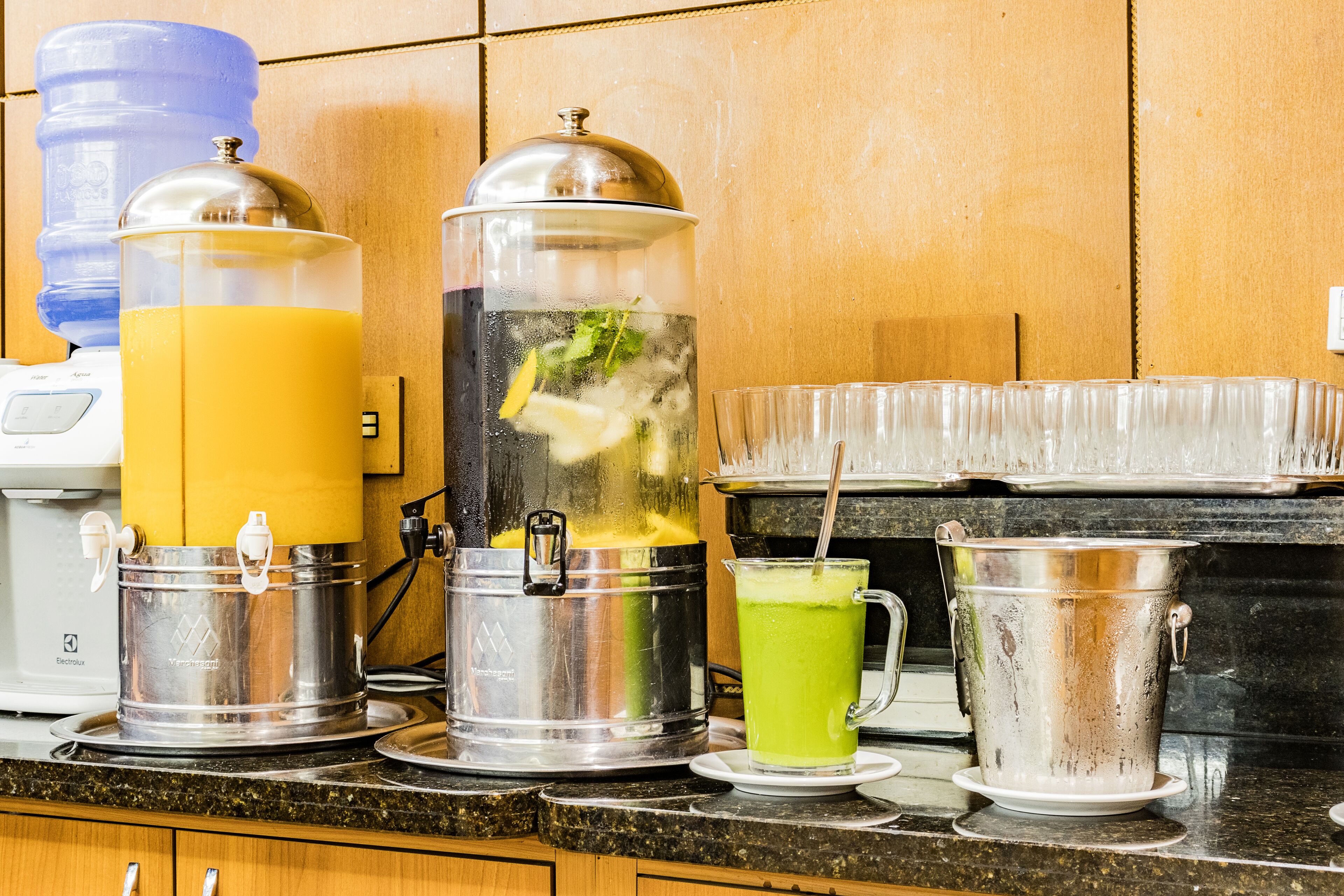 A kitchen counter with a water dispenser, a juicer, and a pitcher with a green drink.