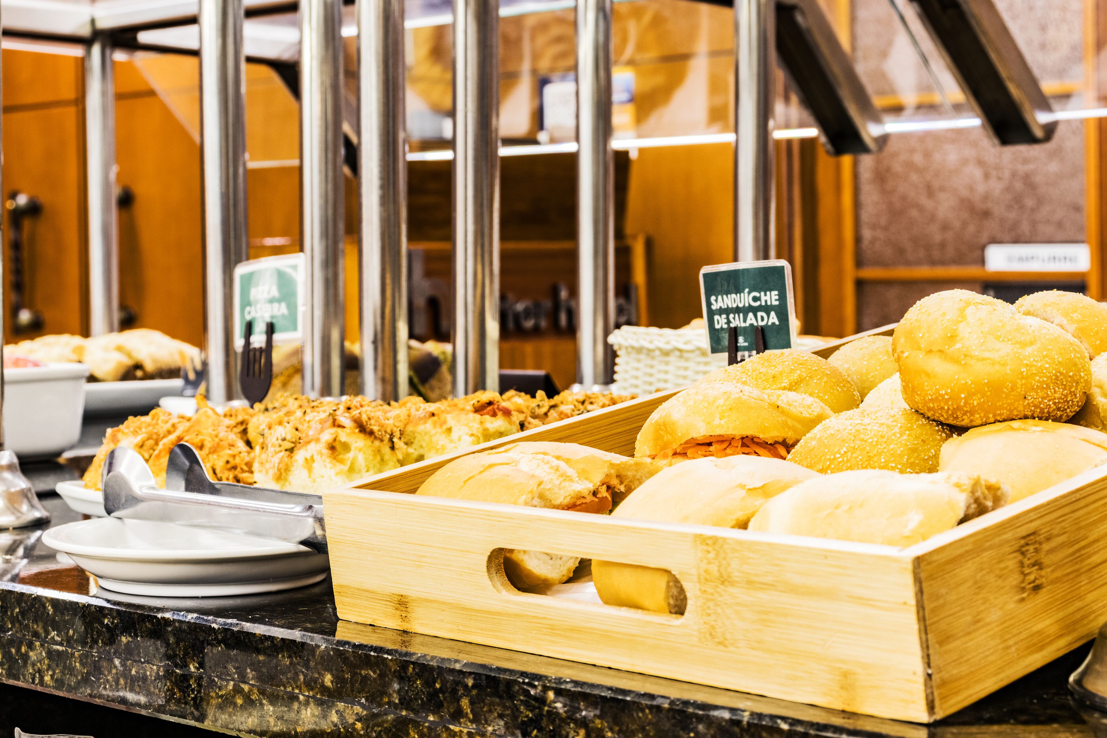 A buffet with various food items including bread rolls and a sign indicating 'SANDWICHES'.