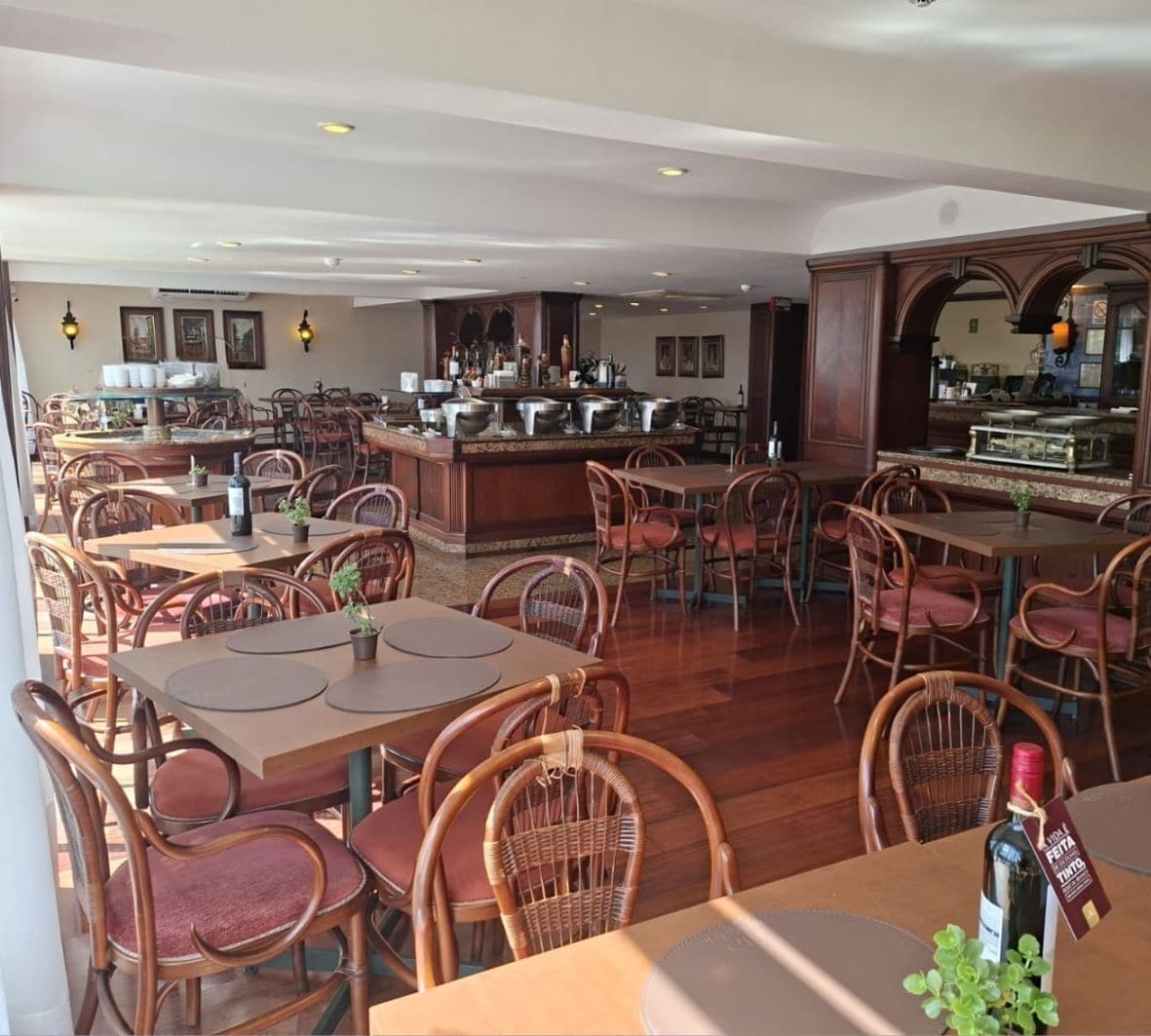 Un restaurante con mesas de madera y sillas de mimbre, una zona de bar y vistas a la cocina.