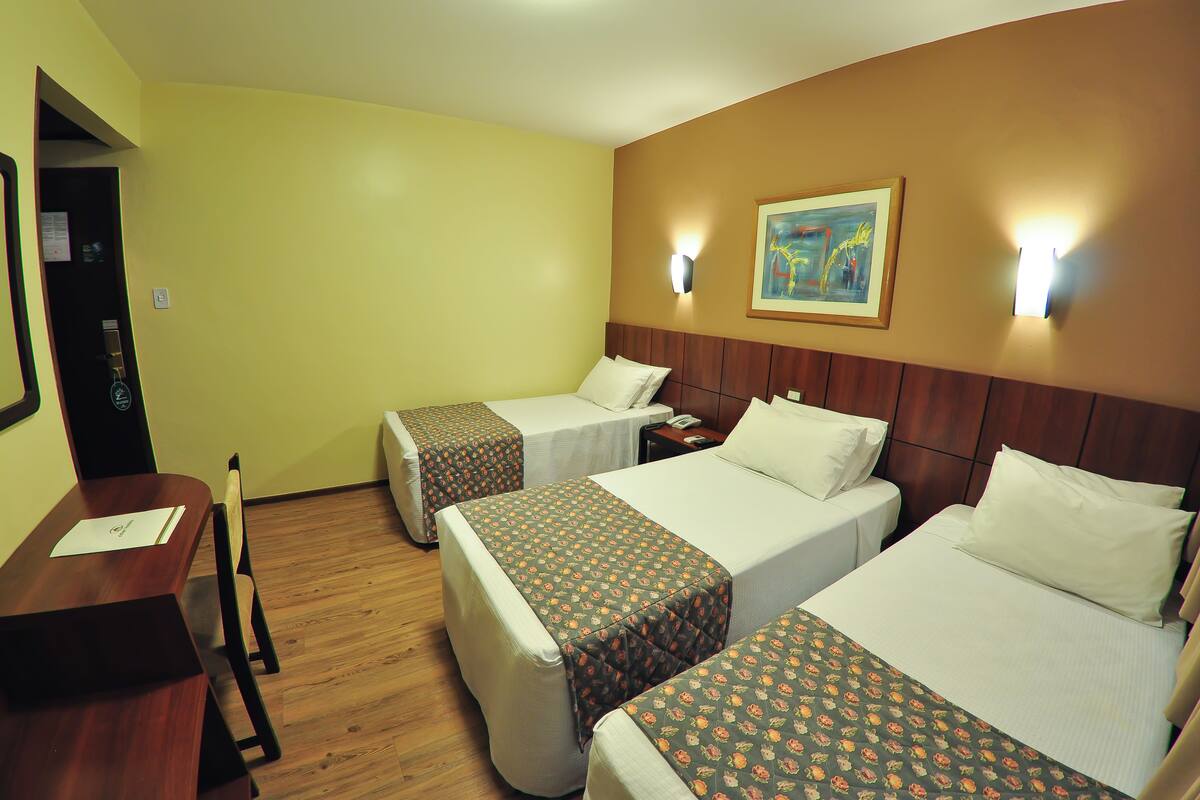 A hotel room with three single beds, a wooden desk, and a chair.
