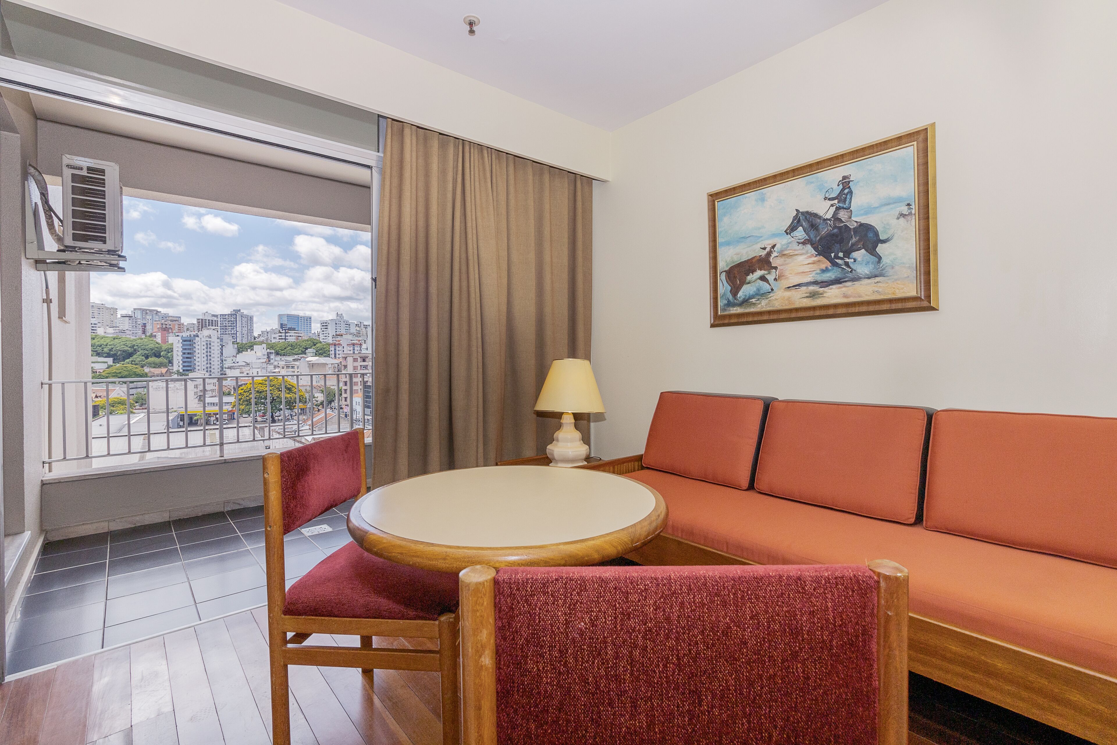 A hotel room with a balcony, a sofa, a round table, and a painting.