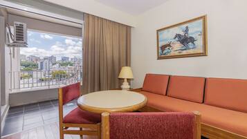 A hotel room with a balcony, a sofa, a round table, and a painting.