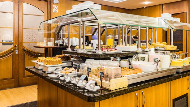 A buffet with various food items and a glass display case. - Ritter Hotéis (Porto Alegre)