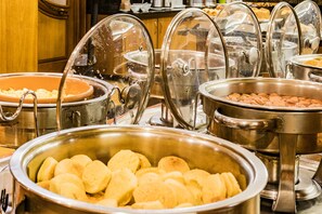 A buffet with various food items in metal serving dishes, covered with glass lids.