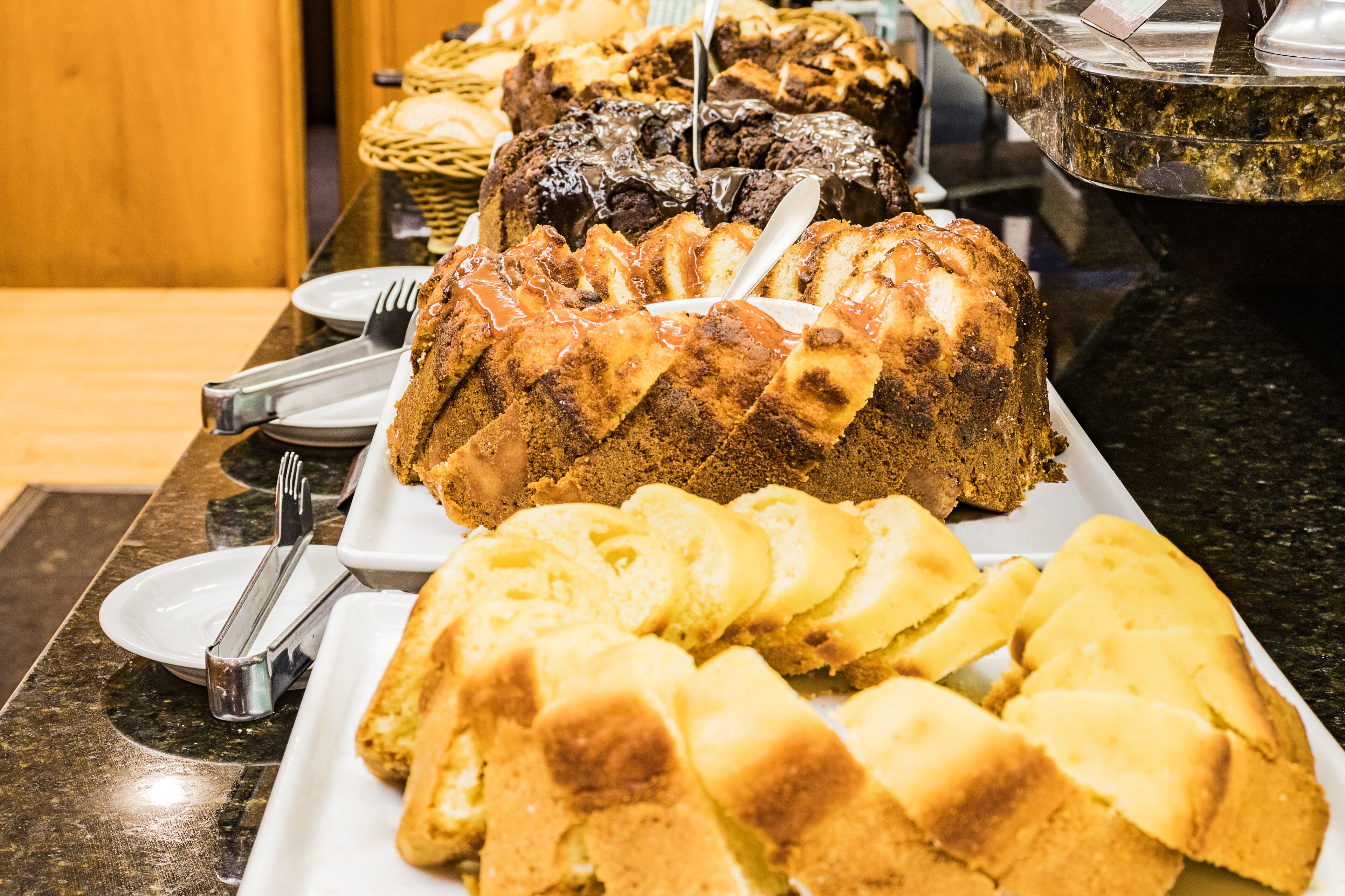 A buffet with various baked goods including a bundt cake, bread rolls, and sliced pastries.