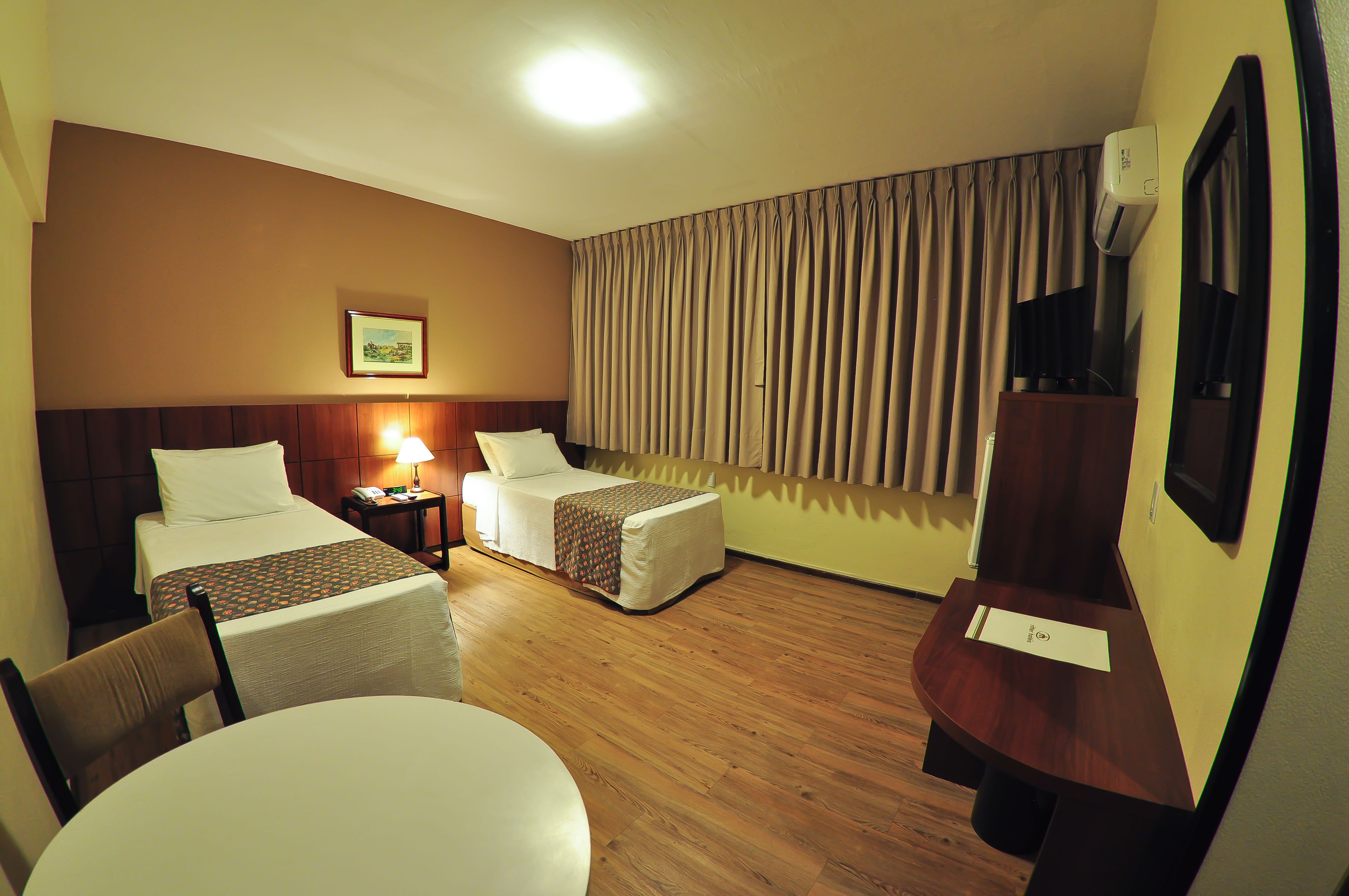 A hotel room with two beds, a desk, a chair, a lamp, and a picture on the wall.