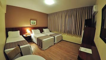 Una habitación de hotel con dos camas individuales, un escritorio, una silla, una lámpara y un ventanal con cortinas.
