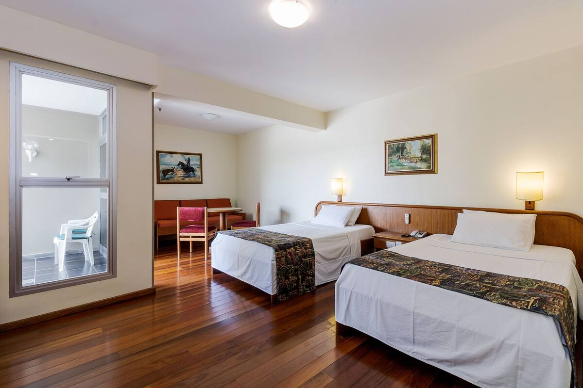 A hotel room with two beds, a desk, a chair, and a window.
