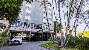 A hotel with a covered entrance, a car parked in front, and tropical vegetation around. - Ritter Hotéis (Porto Alegre)