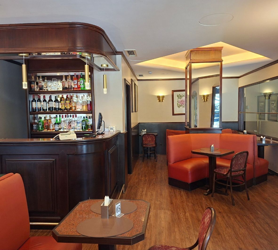 A bar area with a wooden counter, shelves of liquor bottles, and seating including a booth and a table with chairs.
