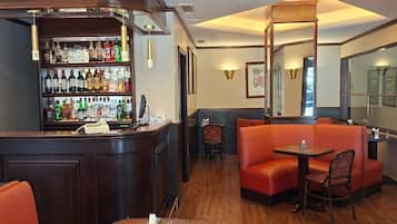 A bar area with a wooden counter, shelves of liquor bottles, and seating including a booth and a table with chairs.