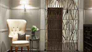 A chair with a cushioned backrest, a small side table with a vase of flowers, and a decorative metal gate with a branch pattern. - Las Alcobas, a Luxury Collection Hotel, Mexico City (Mexico City)