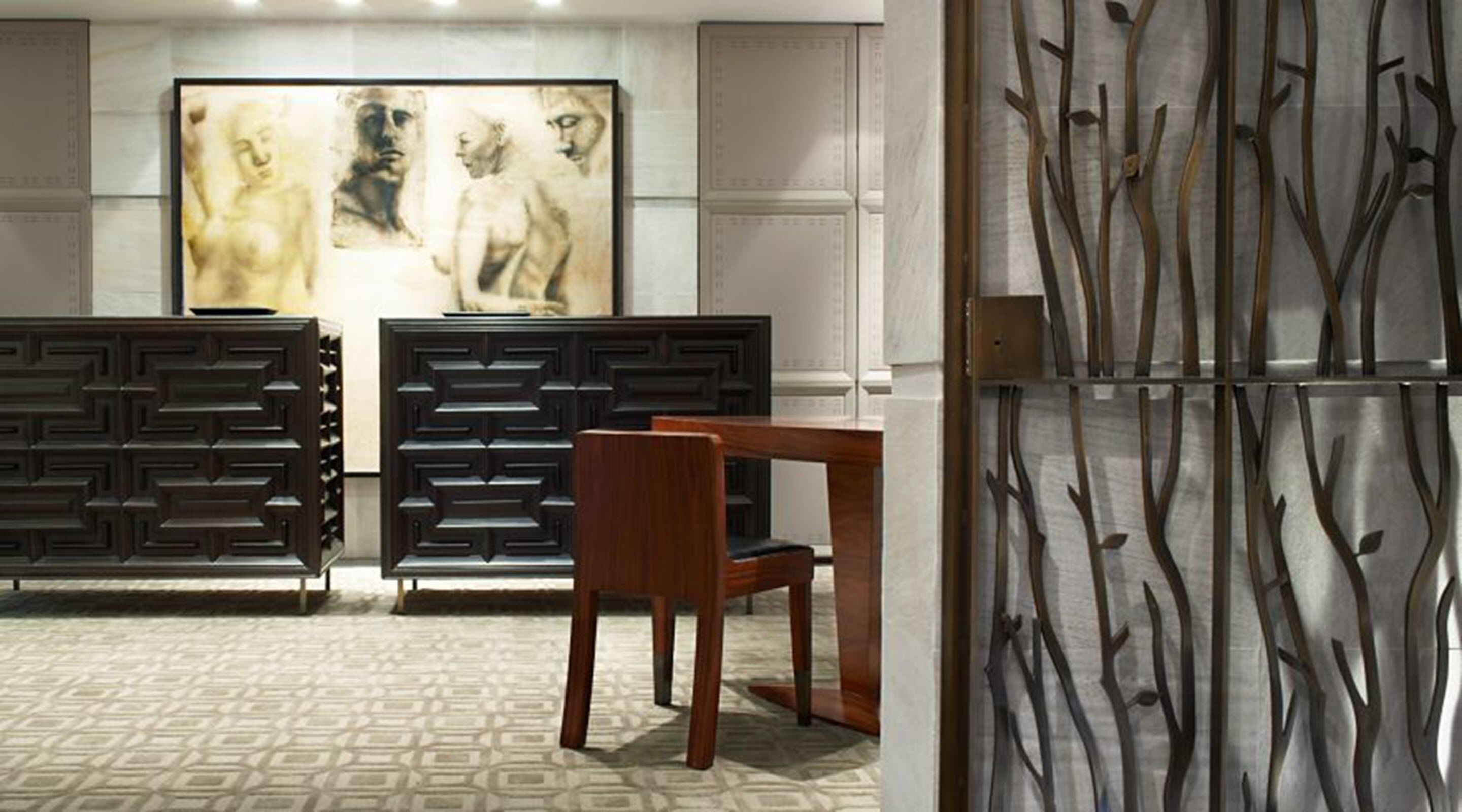 A modern interior with a geometric patterned wall, a wooden dining table, and a decorative panel with abstract branches.
