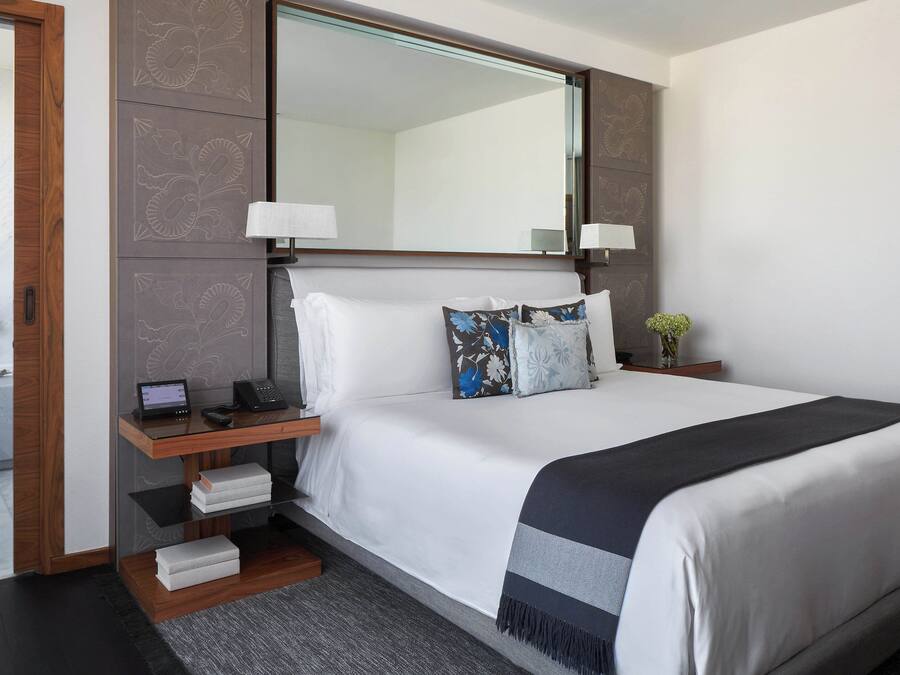 A neatly arranged hotel room with a large bed, bedside tables, a mirror, and a small side table with a lamp.