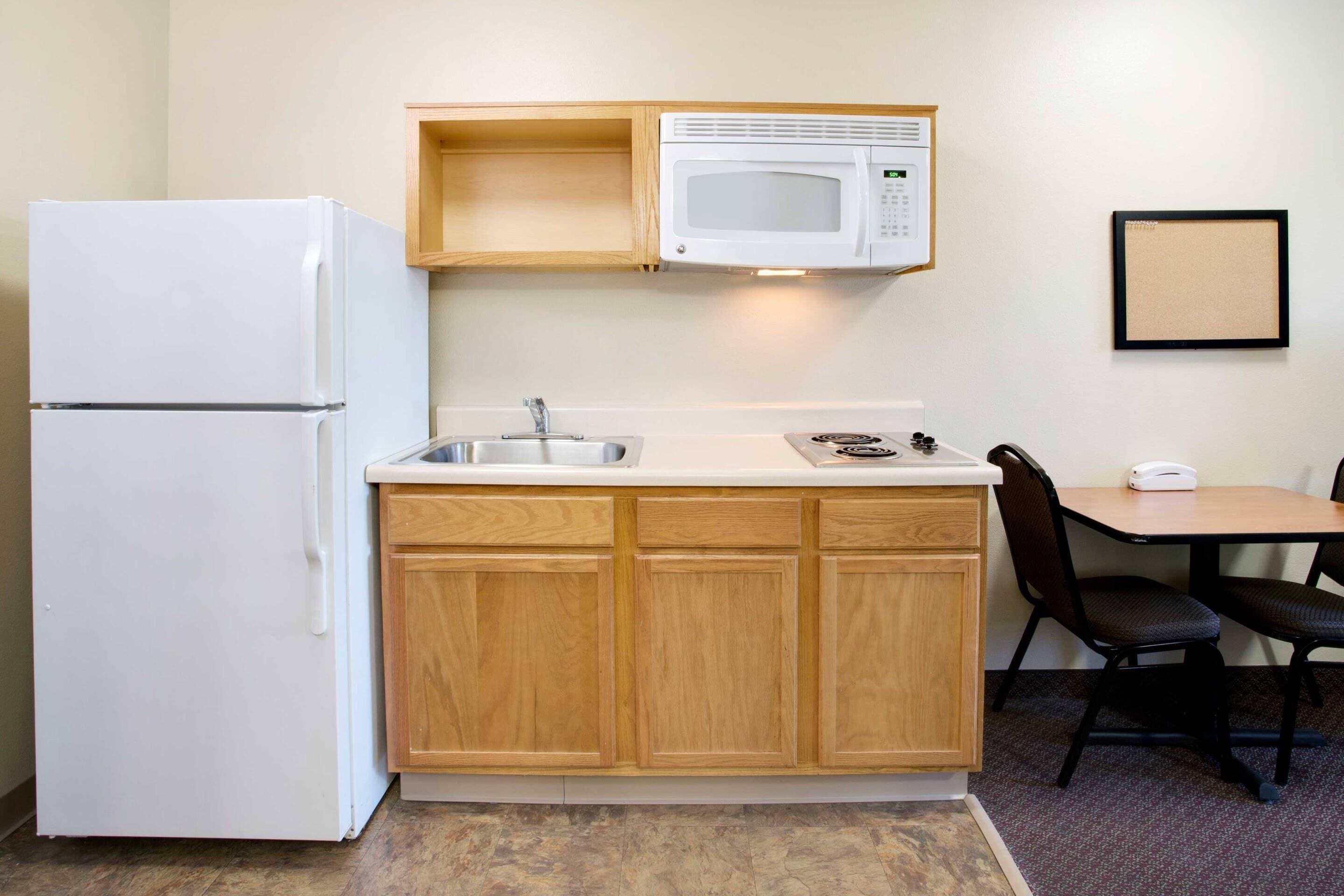 A compact kitchen with a refrigerator, microwave, sink, and wooden cabinets.