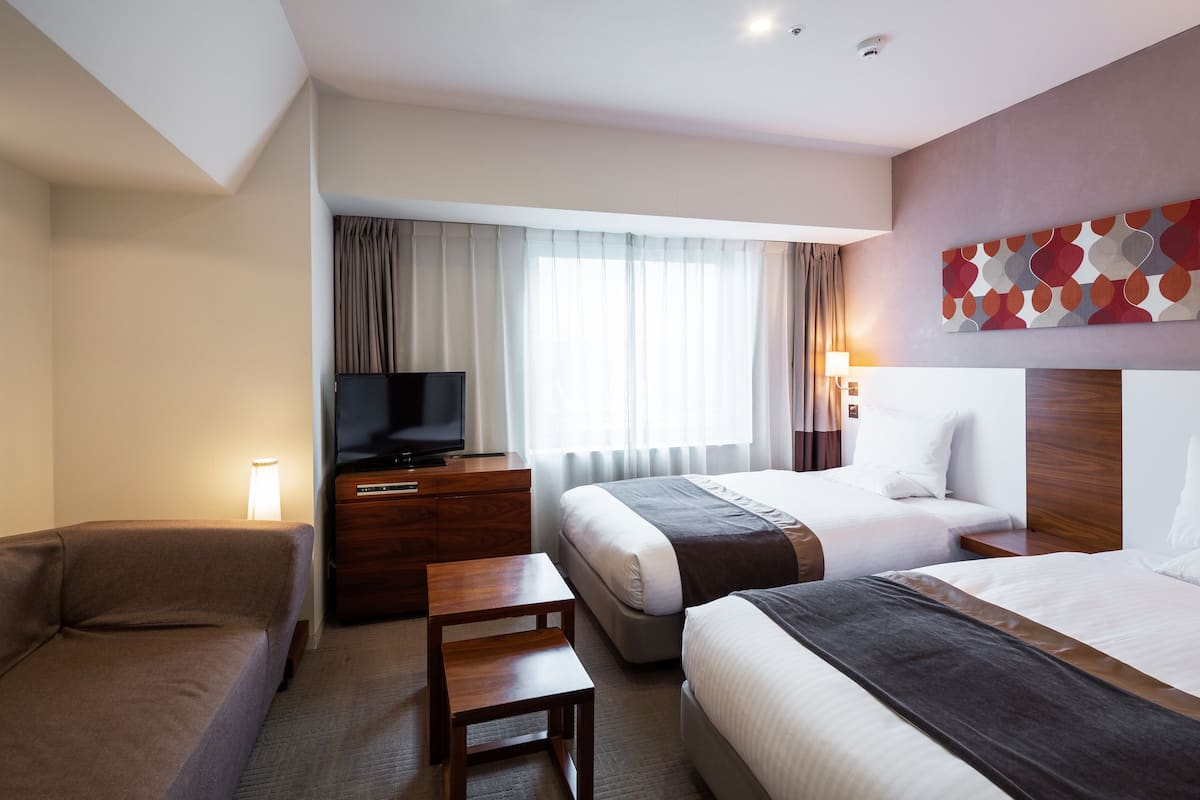 A hotel room with two beds, a TV, a desk, and a sofa.