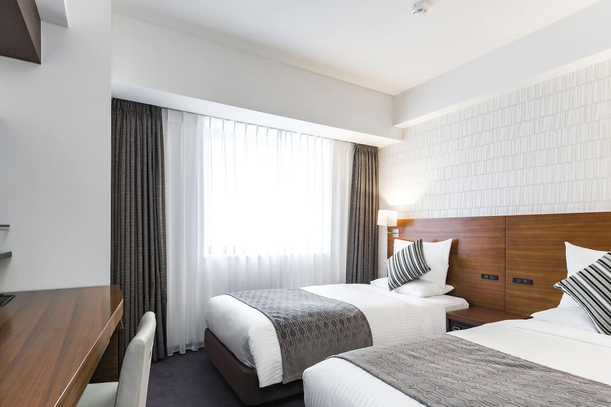A hotel room with two beds, a desk, and a chair.