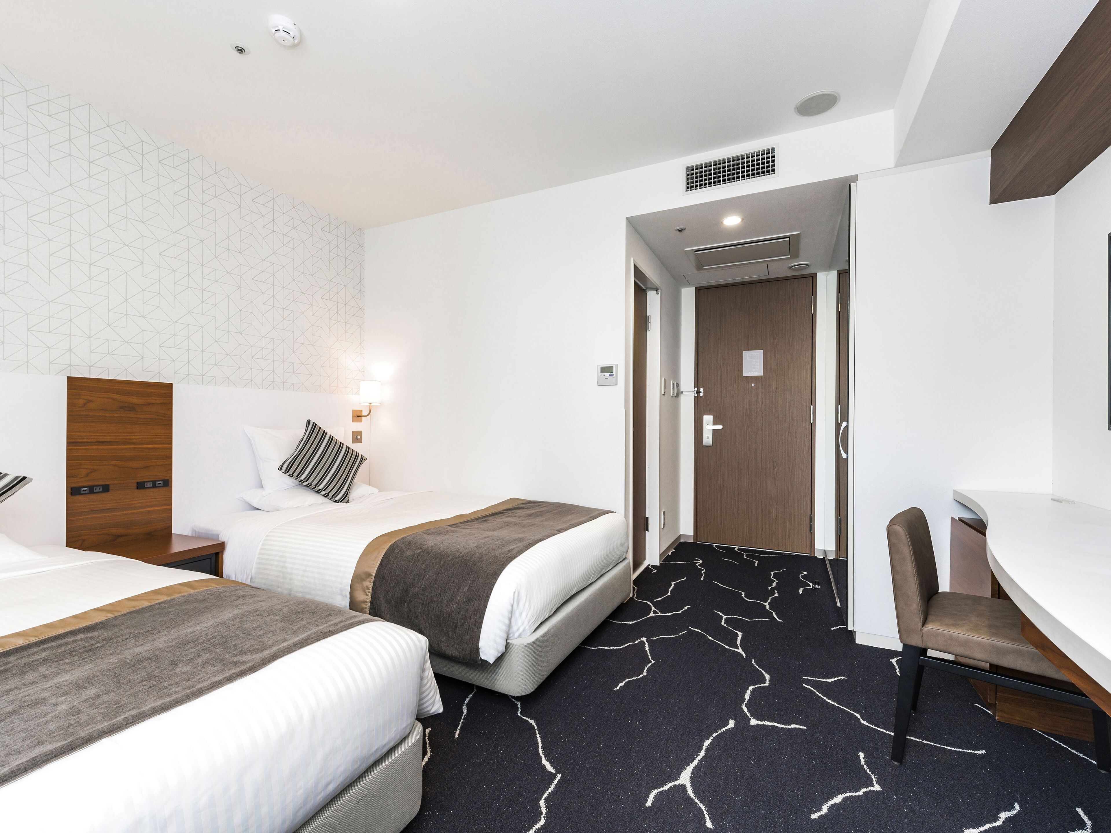 A hotel room with two beds, a desk, and a chair.