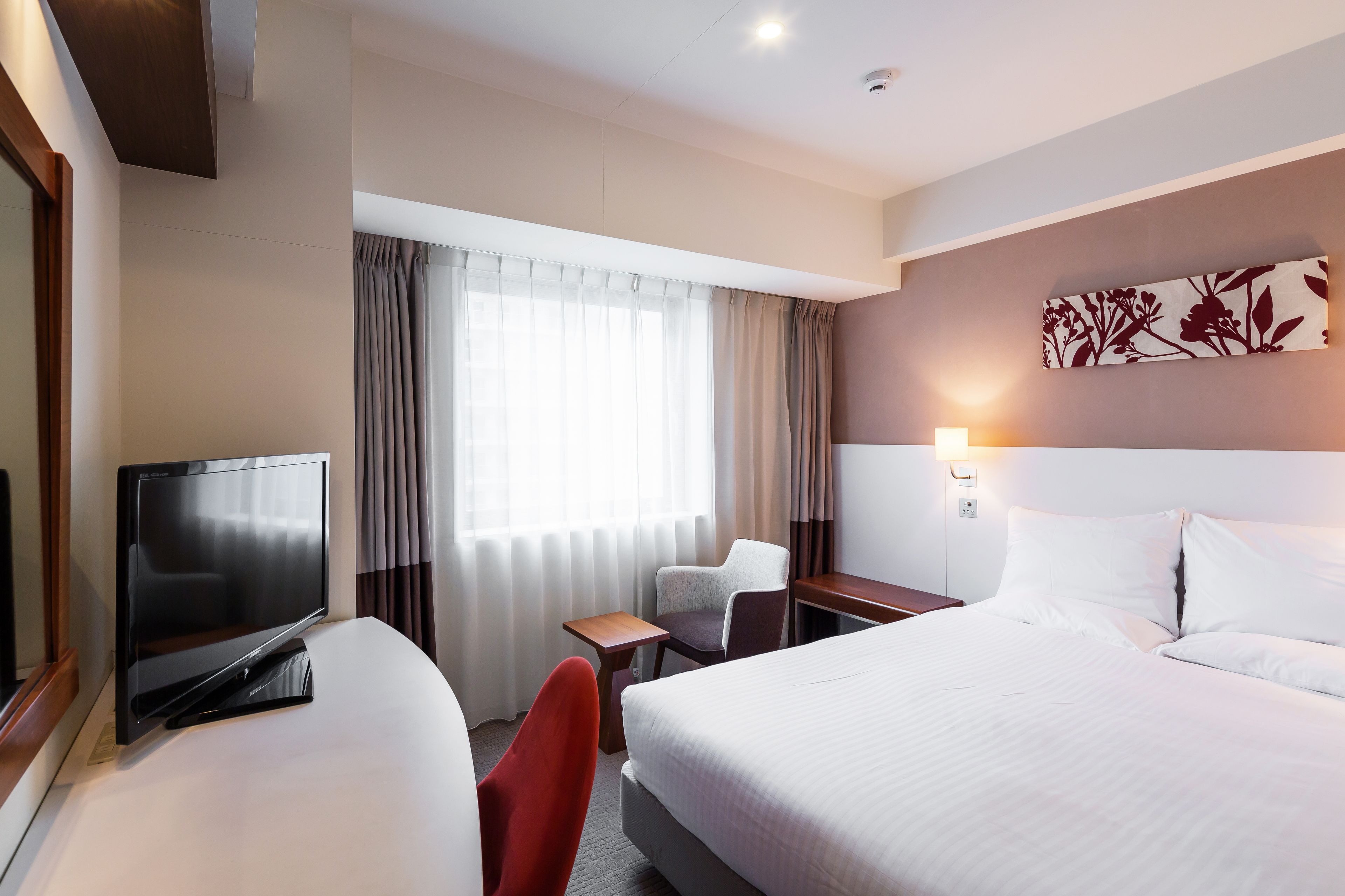 A hotel room with a bed, a TV, a desk, a chair, and a window with curtains.