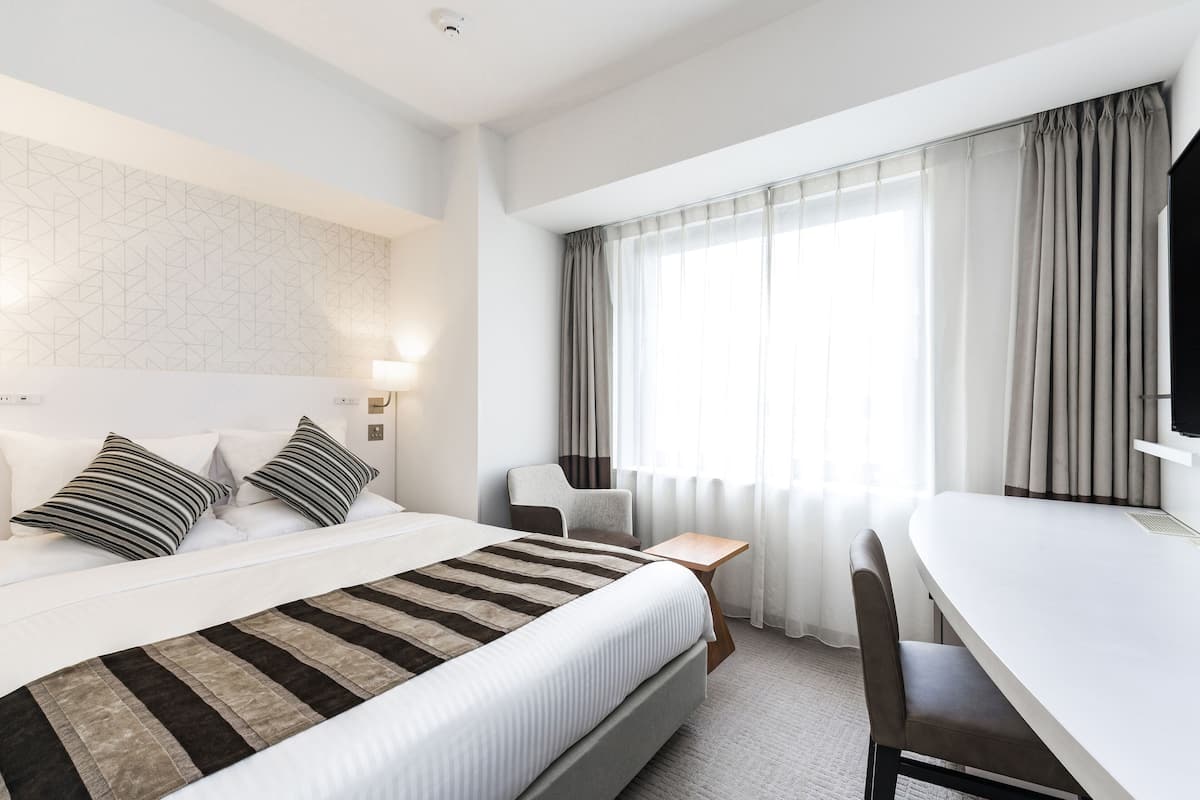 A modern hotel room with a large bed, a desk, and a chair.