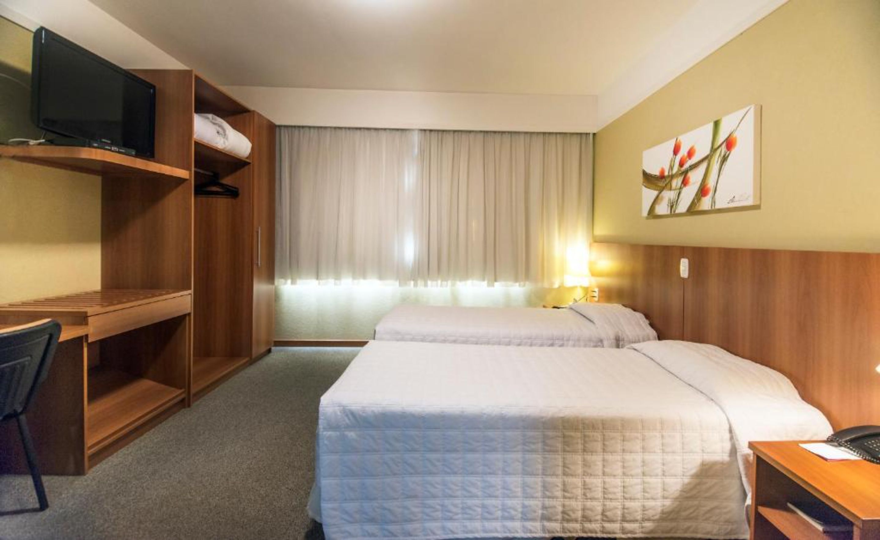 Habitación de hotel con dos camas, un escritorio con televisor y una ventana con cortinas.