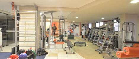 Un gimnasio con varios equipos de ejercicio, incluyendo cintas de correr, máquinas de pesas y pesas libres.