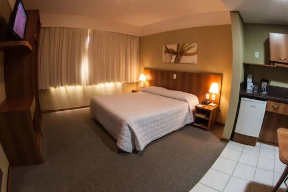 A hotel room with a bed, bedside lamps, a small desk, and a kitchenette.