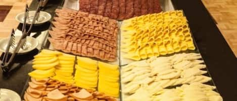 Un bufé con diferentes opciones de comida, incluyendo carnes, quesos y frutas.