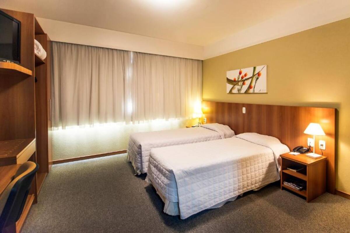 A hotel room with two beds, a TV, a desk, a chair, a lamp, and a painting on the wall.