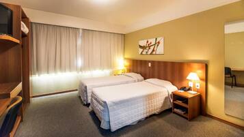 A hotel room with two beds, a TV, a desk, a chair, a lamp, and a painting on the wall.