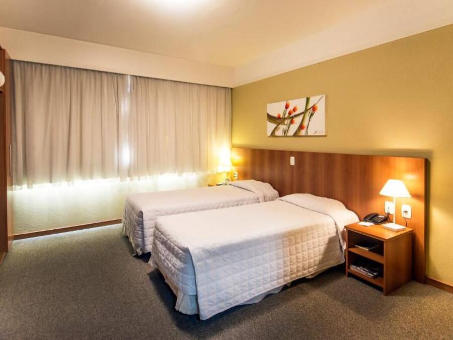 A hotel room with two beds, a TV, a desk, a chair, a lamp, and a painting on the wall.