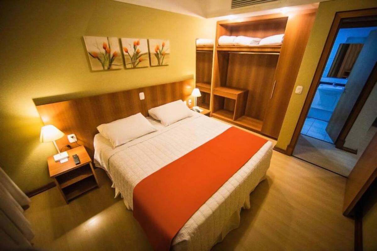 A hotel room with a bed, nightstands, a wardrobe, and artwork on the wall.