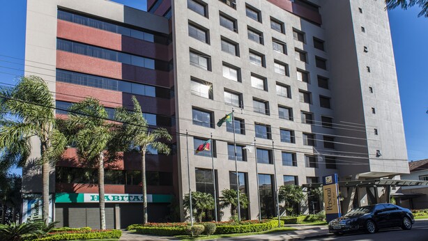 A multi-story hotel with a modern design, featuring a mix of brick and concrete facades, large windows, and a flagpole. - Tri Hotel Executive Caxias (Caxias do Sul)