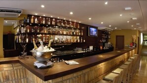 A bar area with a long counter, multiple shelves of bottles, and a television screen mounted on the wall. - Tri Hotel Executive Caxias (Caxias do Sul)