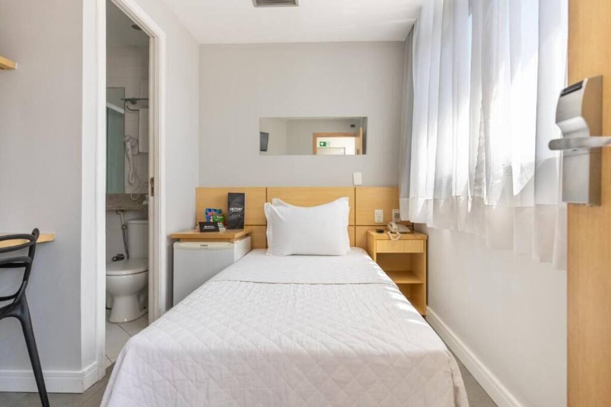 Ein Hotelzimmer mit Bett, Schreibtisch, Stuhl, Nachttisch, Spiegel und Duschbereich.