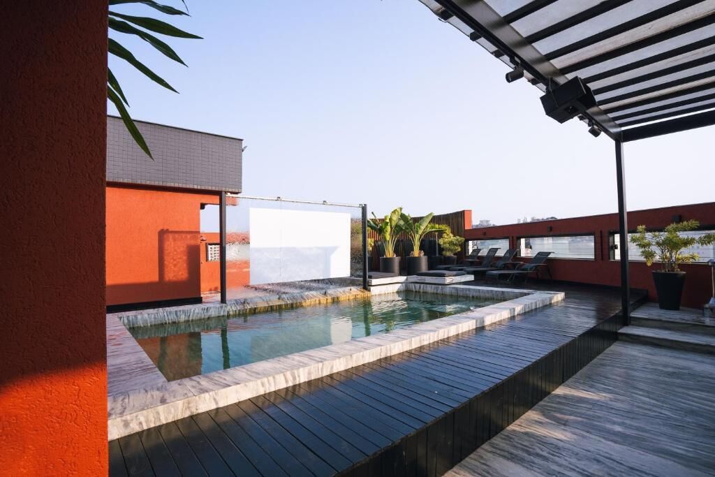 A rooftop pool area with a wooden deck, a white pool, and potted plants.