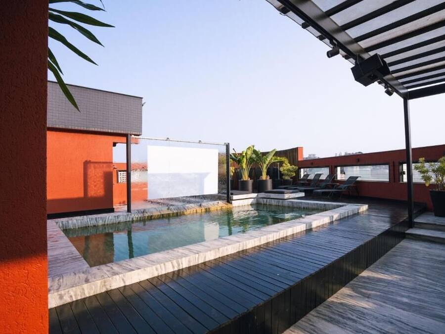 A rooftop pool area with a wooden deck, a white pool, and potted plants.