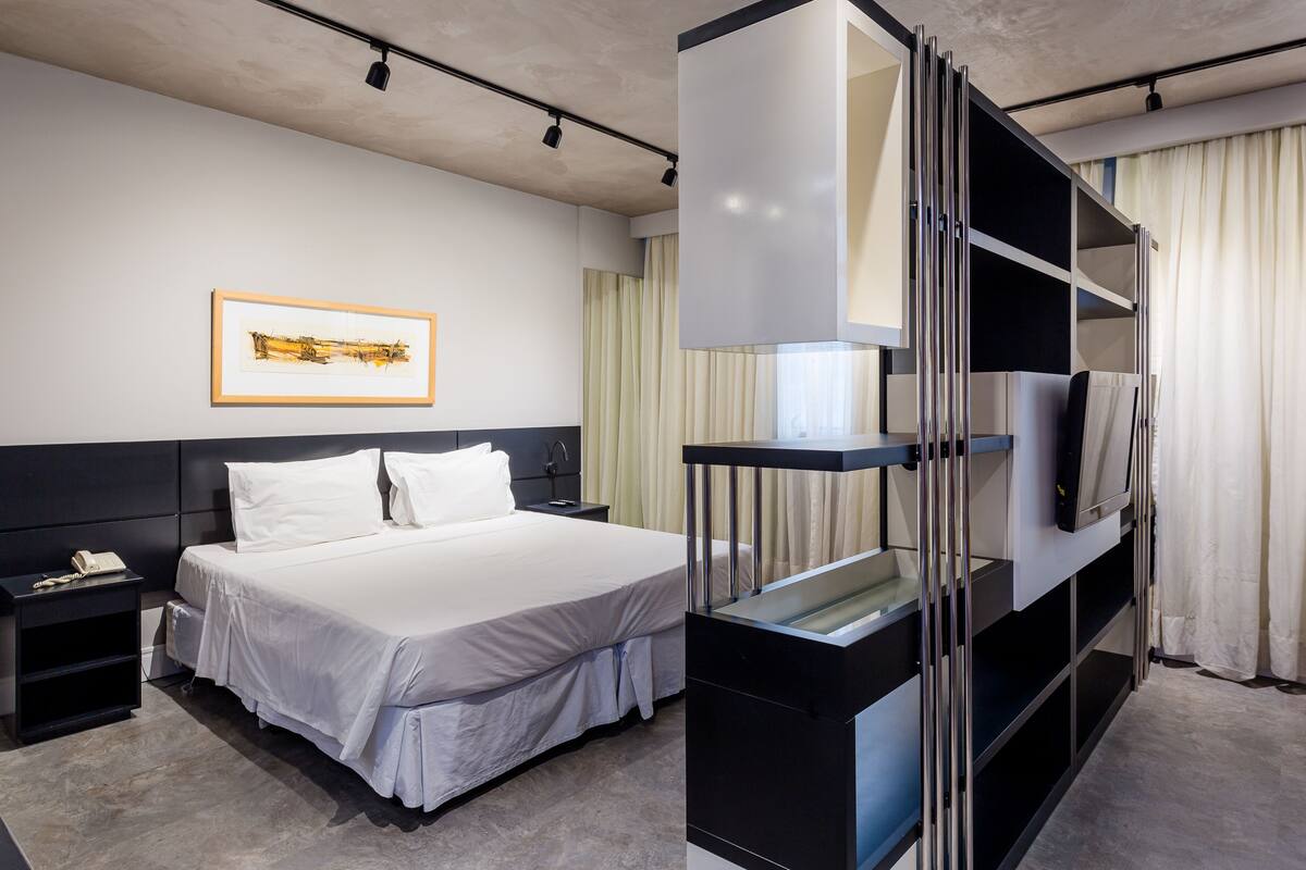 Ein modernes Hotelzimmer mit einem großen Bett, einem Nachttisch mit Telefon, einem gerahmten Kunstwerk an der Wand und einem Fernseher auf einem Tisch.
