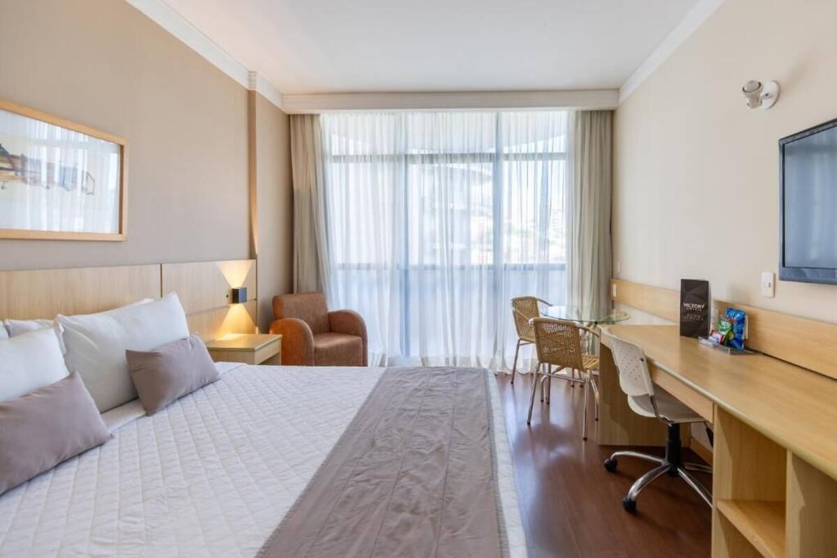 Ein Hotelzimmer mit einem großen Bett, einem Schreibtisch, einem Sessel und einem Fernseher.