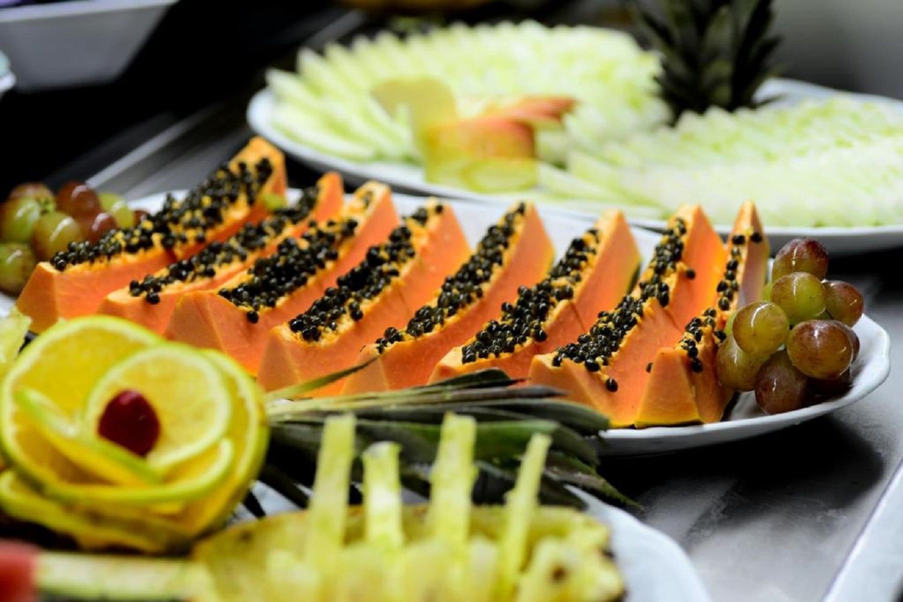 Diversa variedad de frutas cortadas, incluyendo papaya y piña, sobre una mesa de buffet.